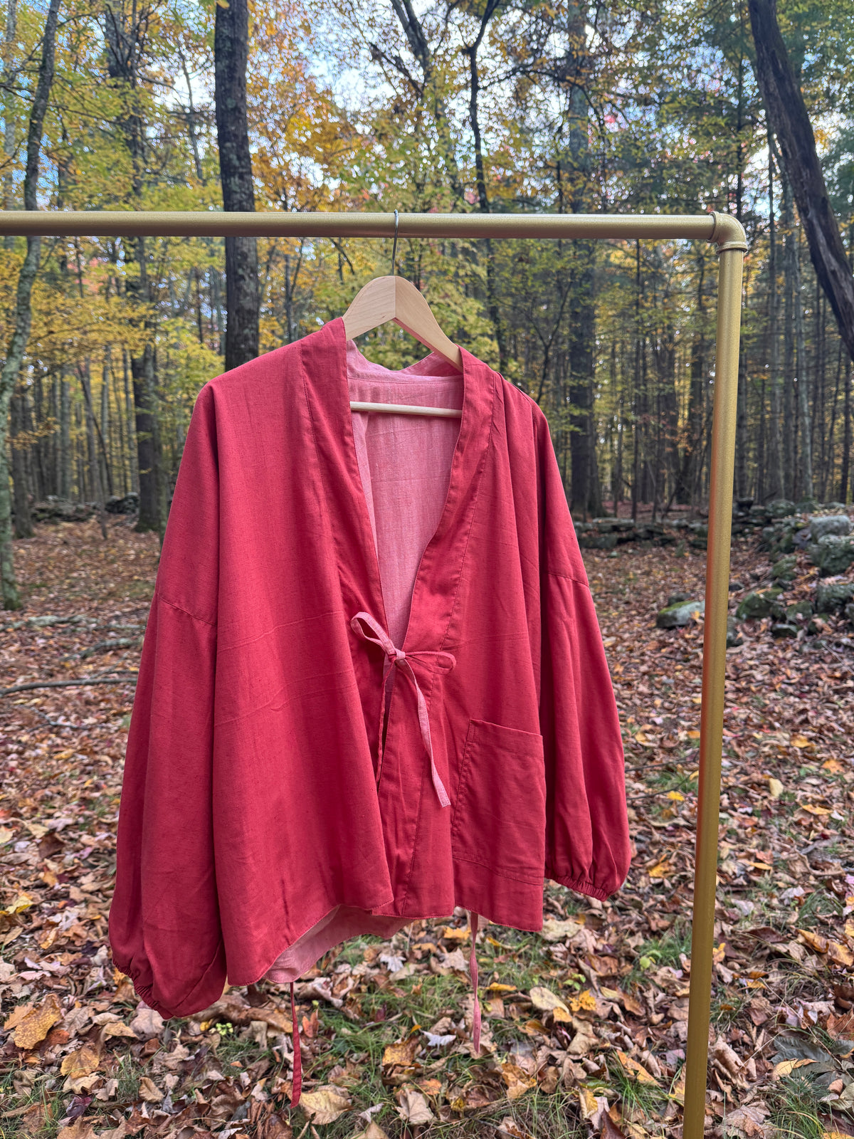 Red reversible wrap jacket hanging on a gold rack in an autumn forest, pink lining showing
