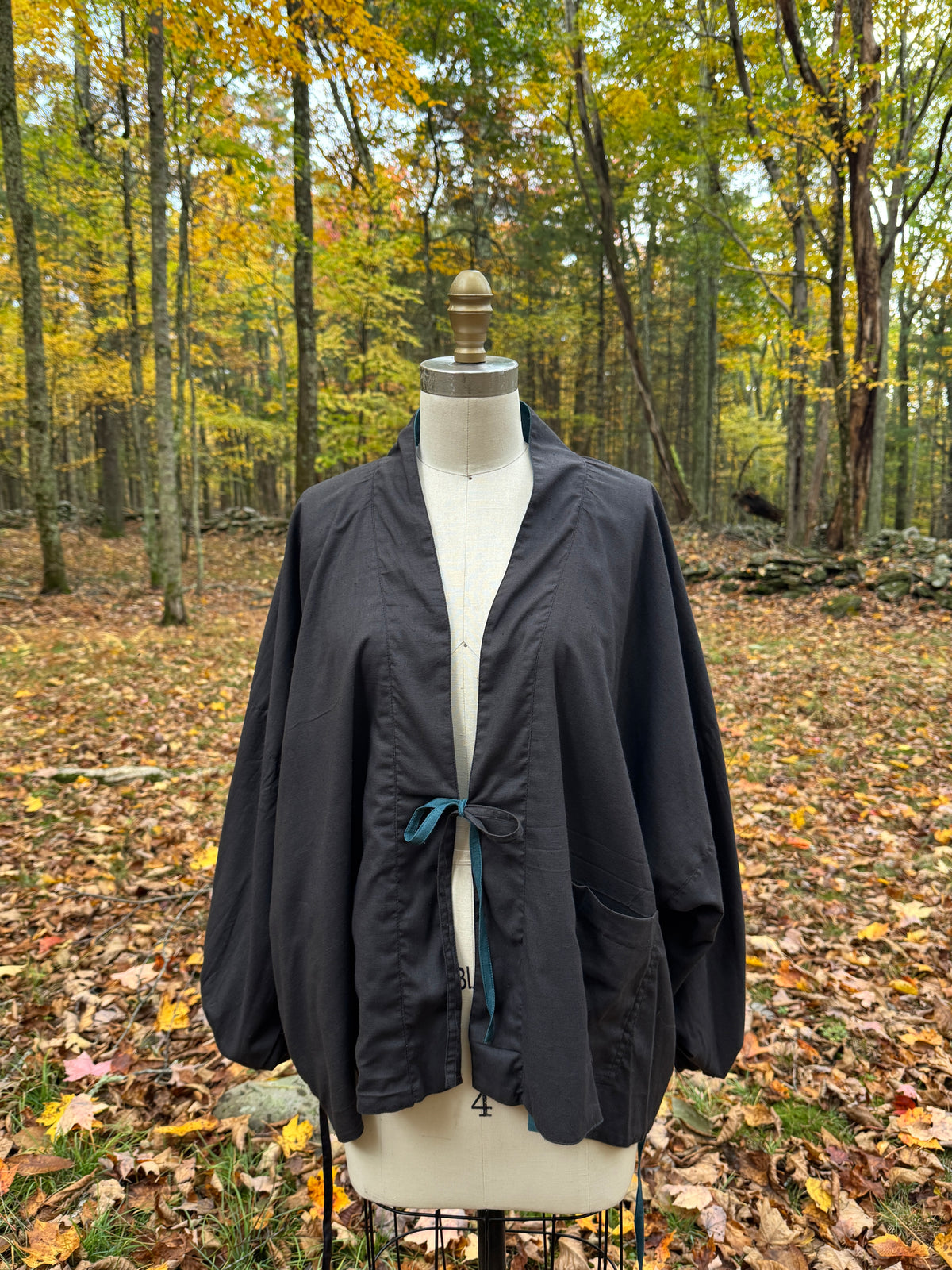 Reversible wrap jacket worn black side out, tied at the center with a teal tie