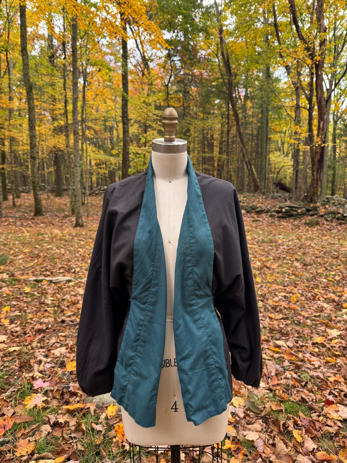 Reversible wrap jacket worn black side out and open, with the teal facing showing down the front